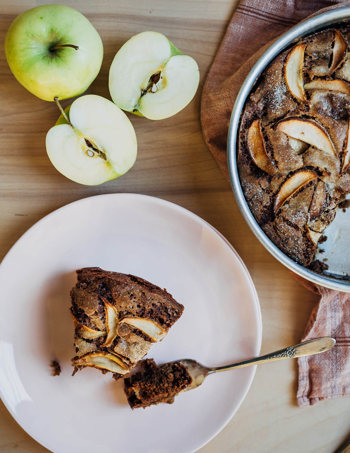Apples, a slice of apple cake, and a cake pan. 