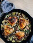 A skillet with golden chicken thighs and vegetables.