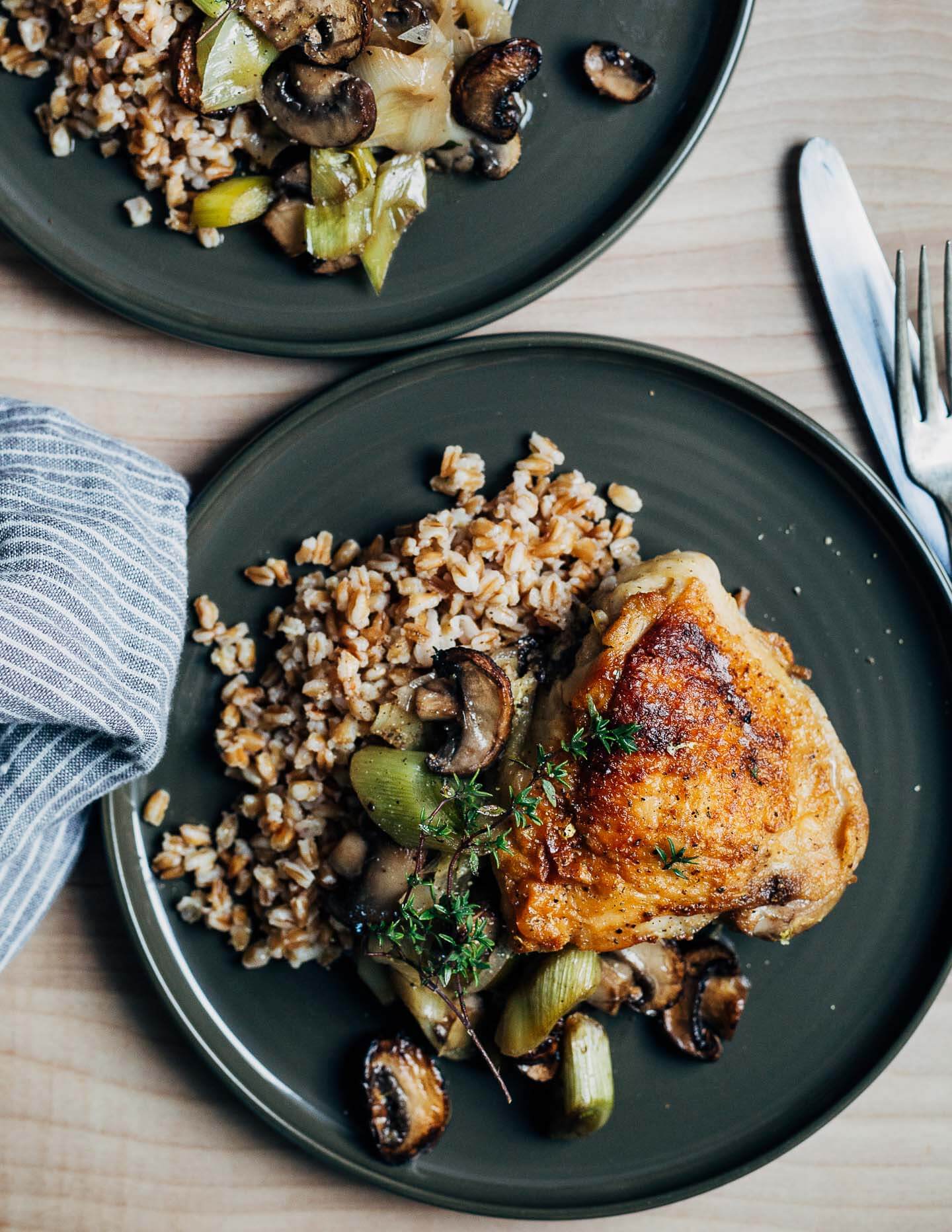 Two plates with grain, vegetables, and chicken thighs. 