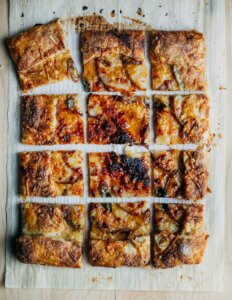 A tart siting on parchment, sliced into 12 squares.