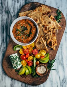 A serving board with dip, naan, veggies, and chèvre.