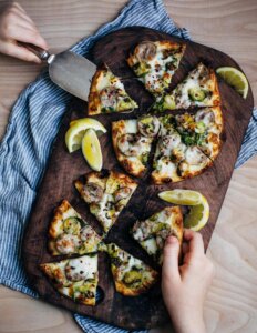 A cutting board with two little pizzas and hands getting slices.