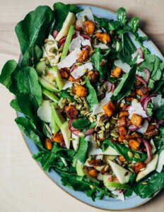 A platter with a big arugula, apple, and butternut squash salad.
