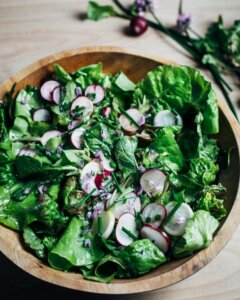 A wooden bowl with a green salad dotted with sliced radishes.
