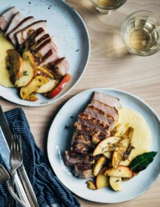 Two plates with polenta, sliced pork and apples.