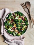 A bowl with broccoli salad with a napkin and serving utensils alongside.
