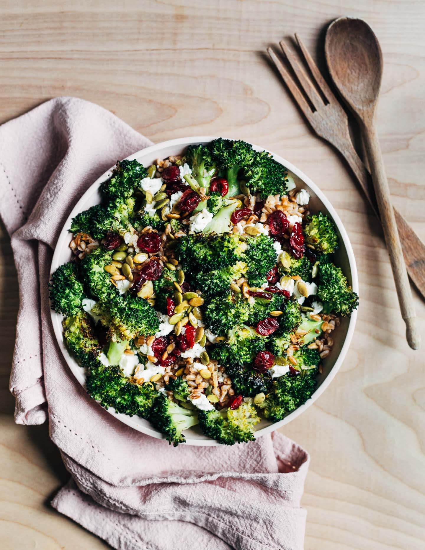 A bowl with broccoli salad with a napkin and serving utensils alongside. 