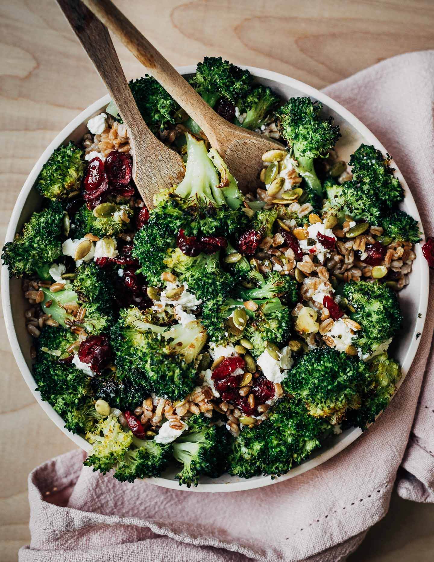 A bowl with broccoli salad with a napkin and serving utensils. 