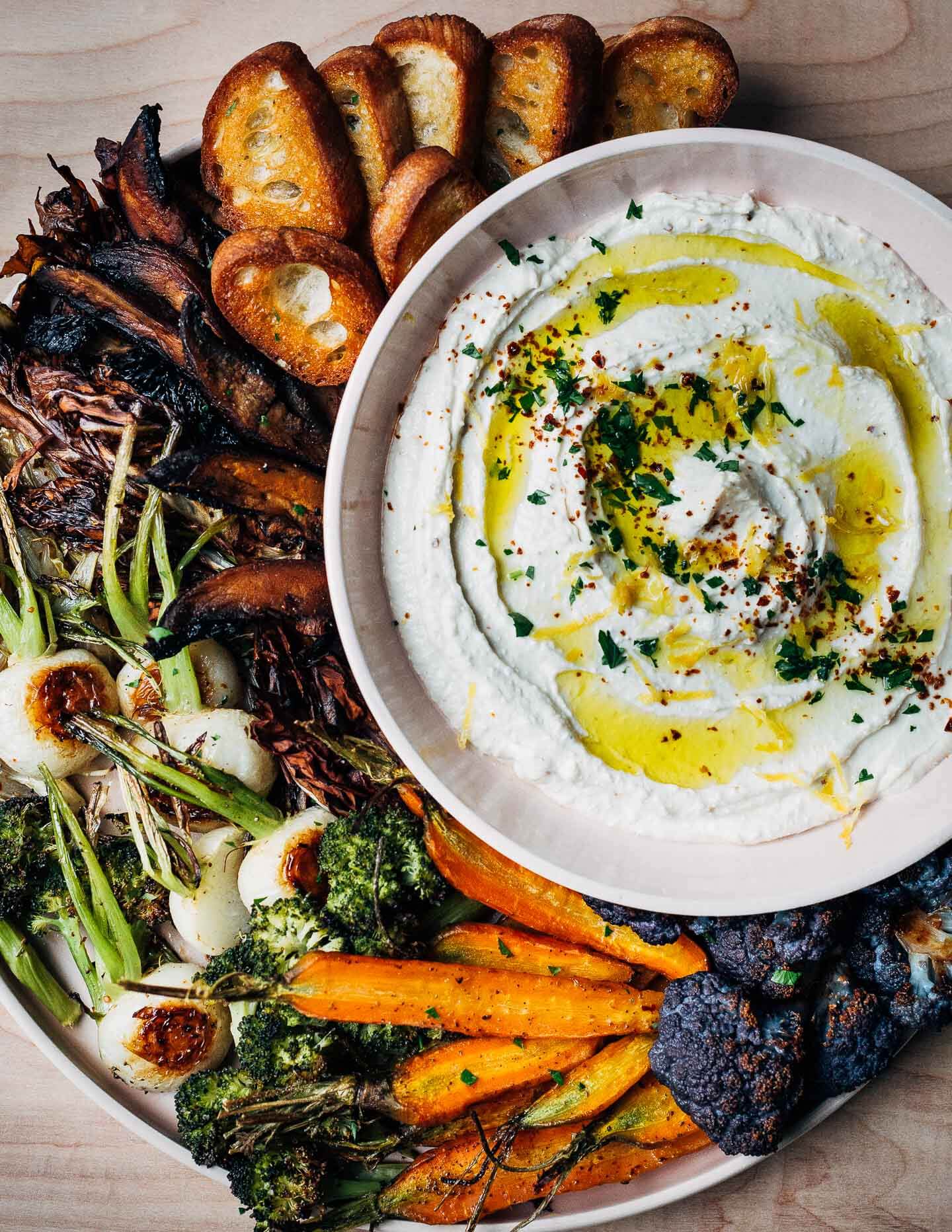 A bowl of dip surrounded by roasted vegetables.