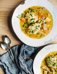 Two bowl of chicken and dumpling soup sprinkled with minced herbs.