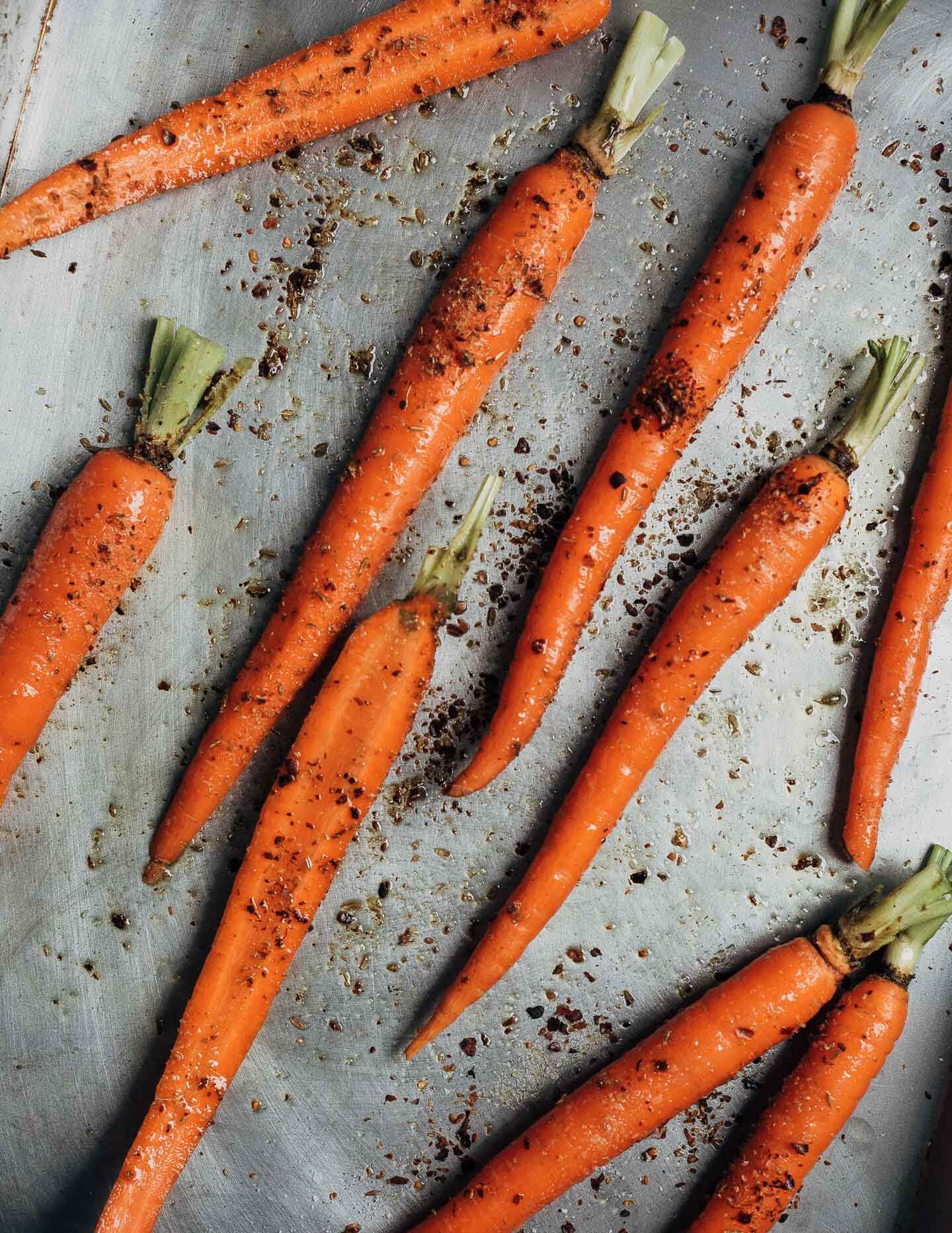 Carrots scattered on a baking sheet with salt and spices. 