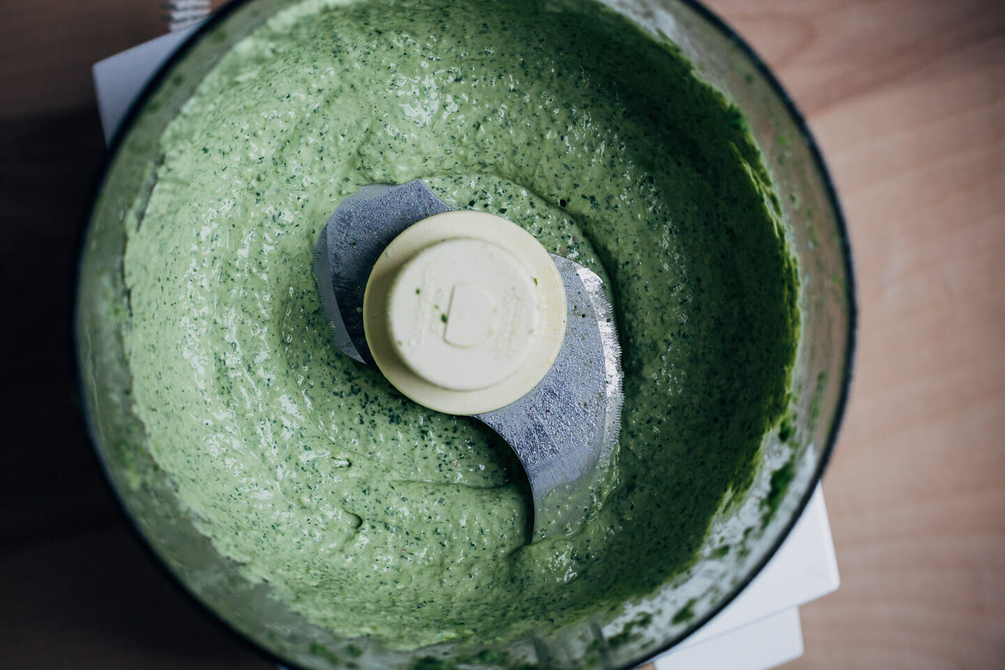 Looking down into a food processor with a green thini mixture inside. 