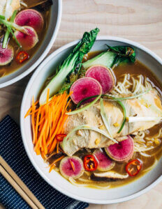 Two bowls of colorful soup with steam chicken and vegetables.