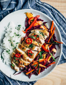 A plate with rice, chicken breast, and red cabbage slaw.
