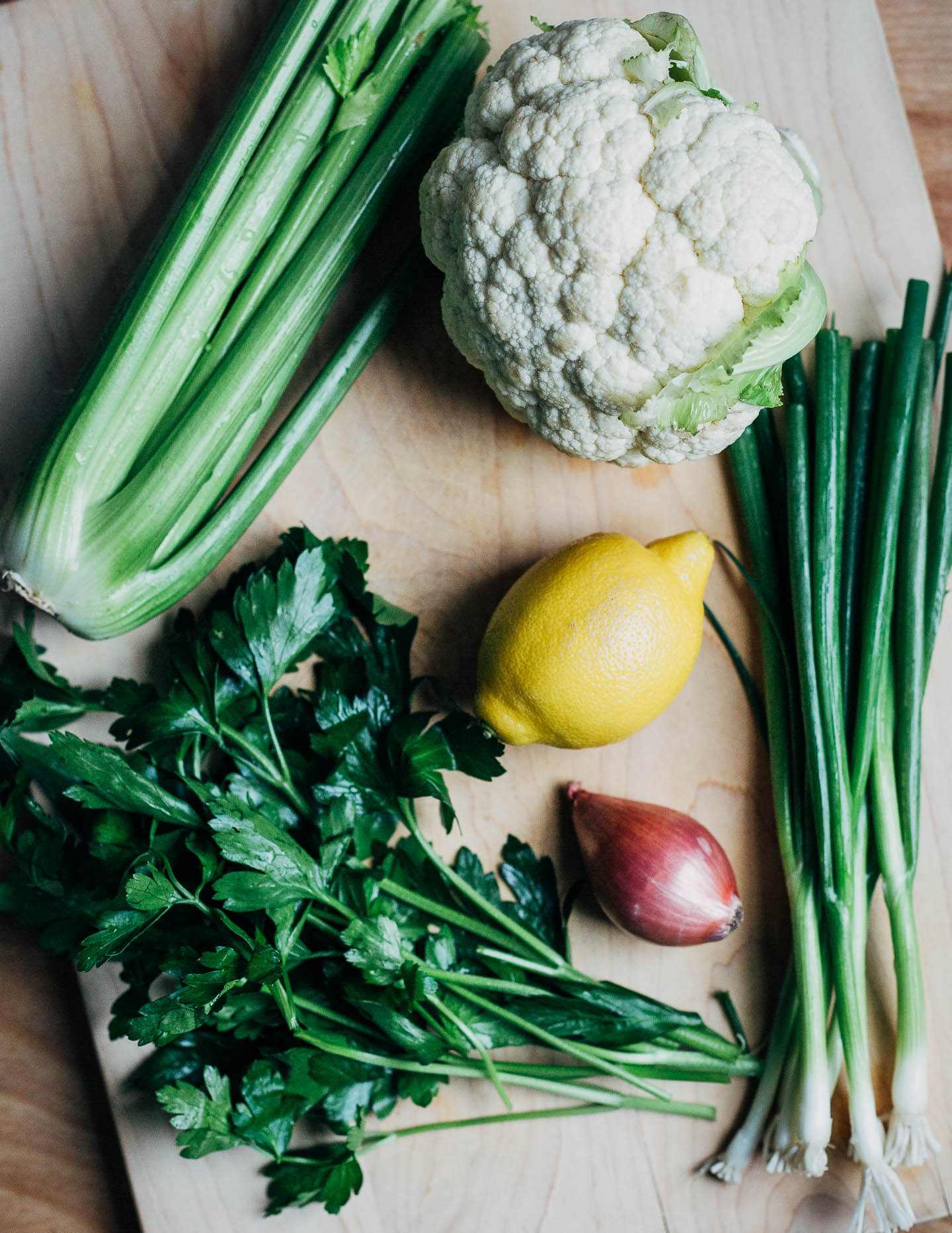A cutting board with celery, cauliflower, parsley, lemon, and shallot. 
