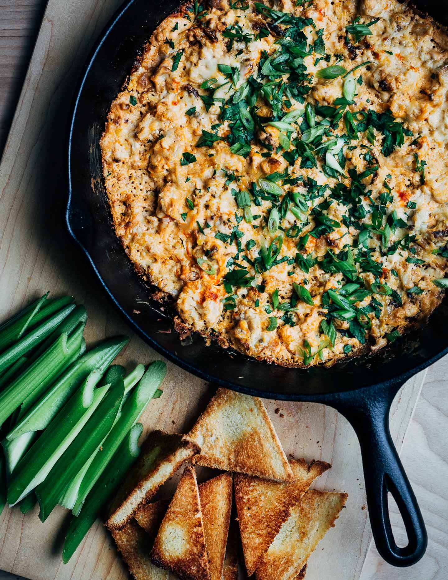 A skillet filled with dip, with toasts and celery on the side. 