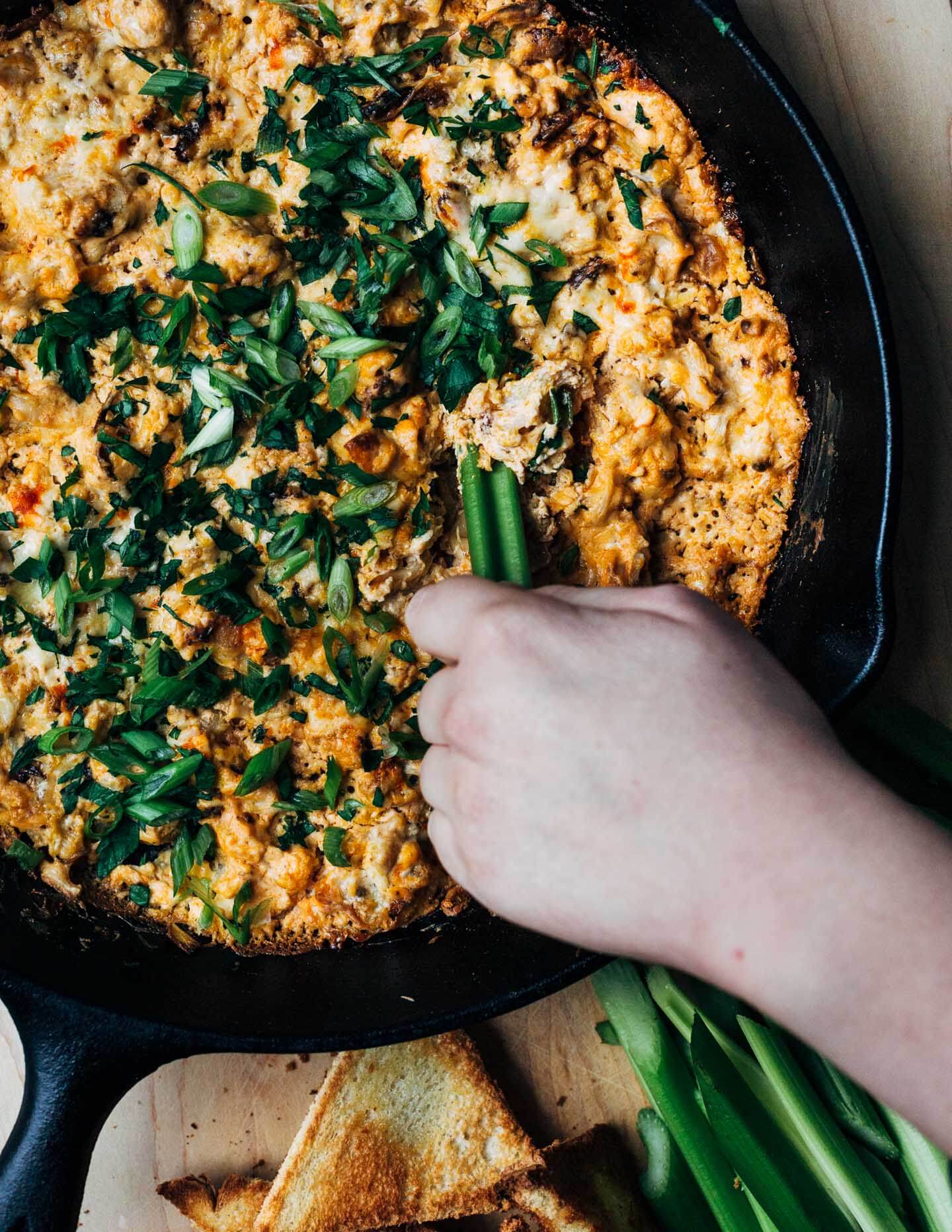 A hand scooping dip from a skillet. 