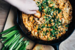 A hand scooping dip from a cast iron skillet.