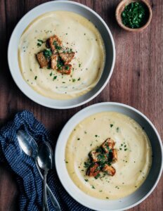 Two bowls of celery roots and rutabaga soup with croutons and herbs.