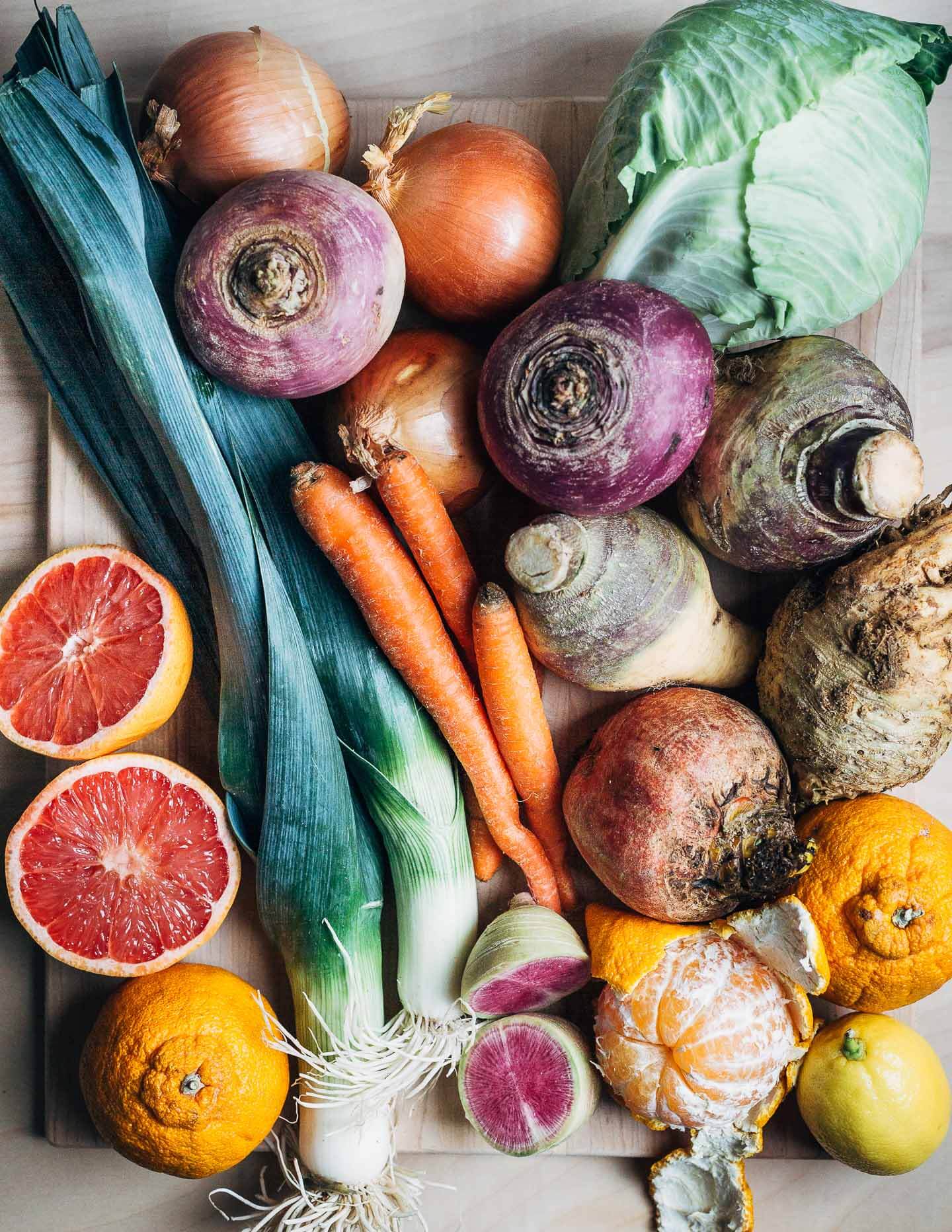 A table piled with leeks, cabbage, citrus, carrots, and root vegetables. 