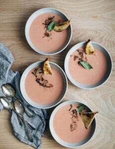 Four bowls of pink radish soup with toasts and onions on top.