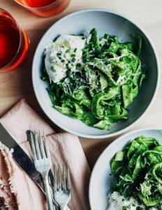 Plates of pasta tossed in a green kale sauce and garnished with burrata.