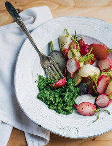 A bowl of roasted turnips and radishes with pesto alongside.