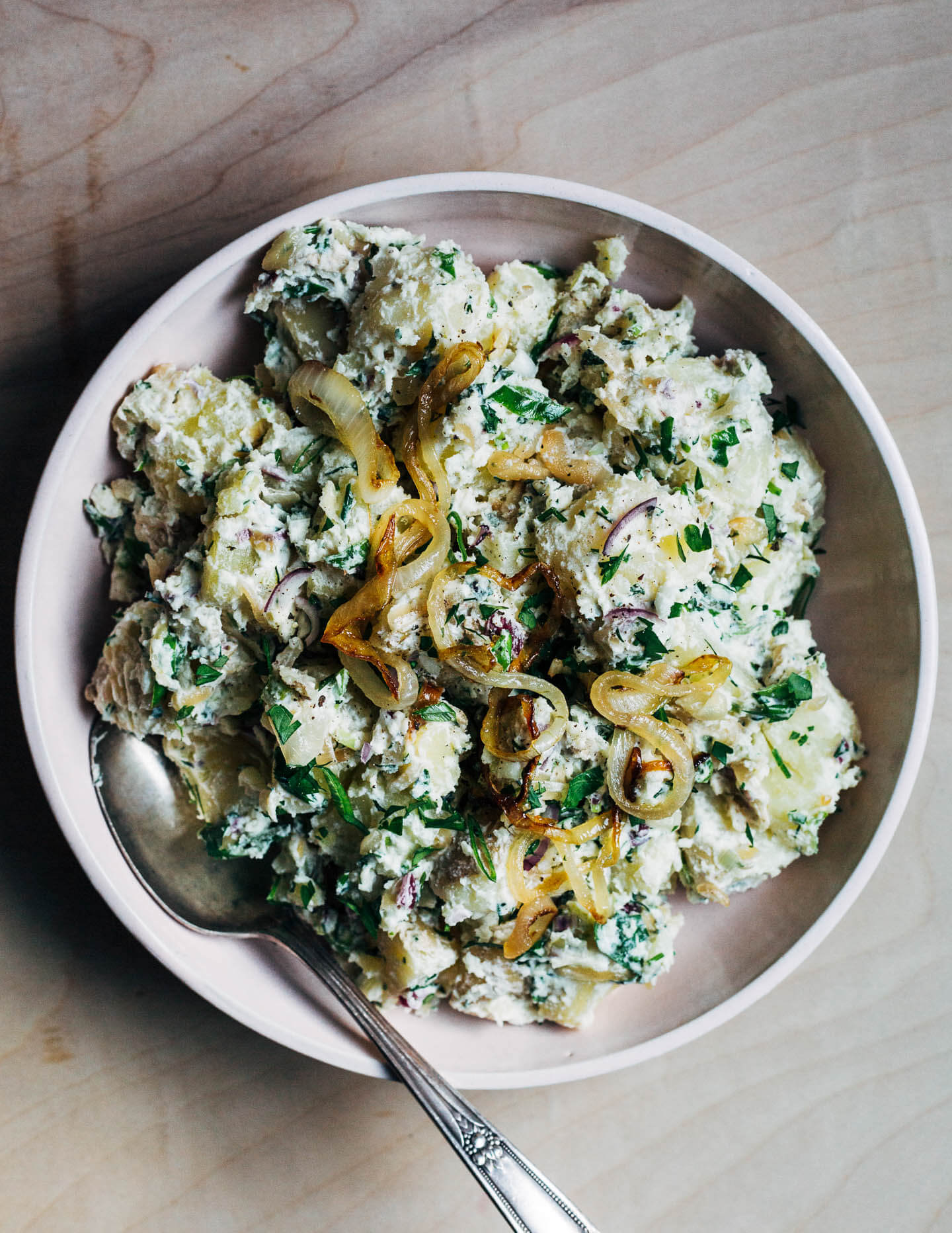 A bowl of herby potato salad with a serving spoon. 
