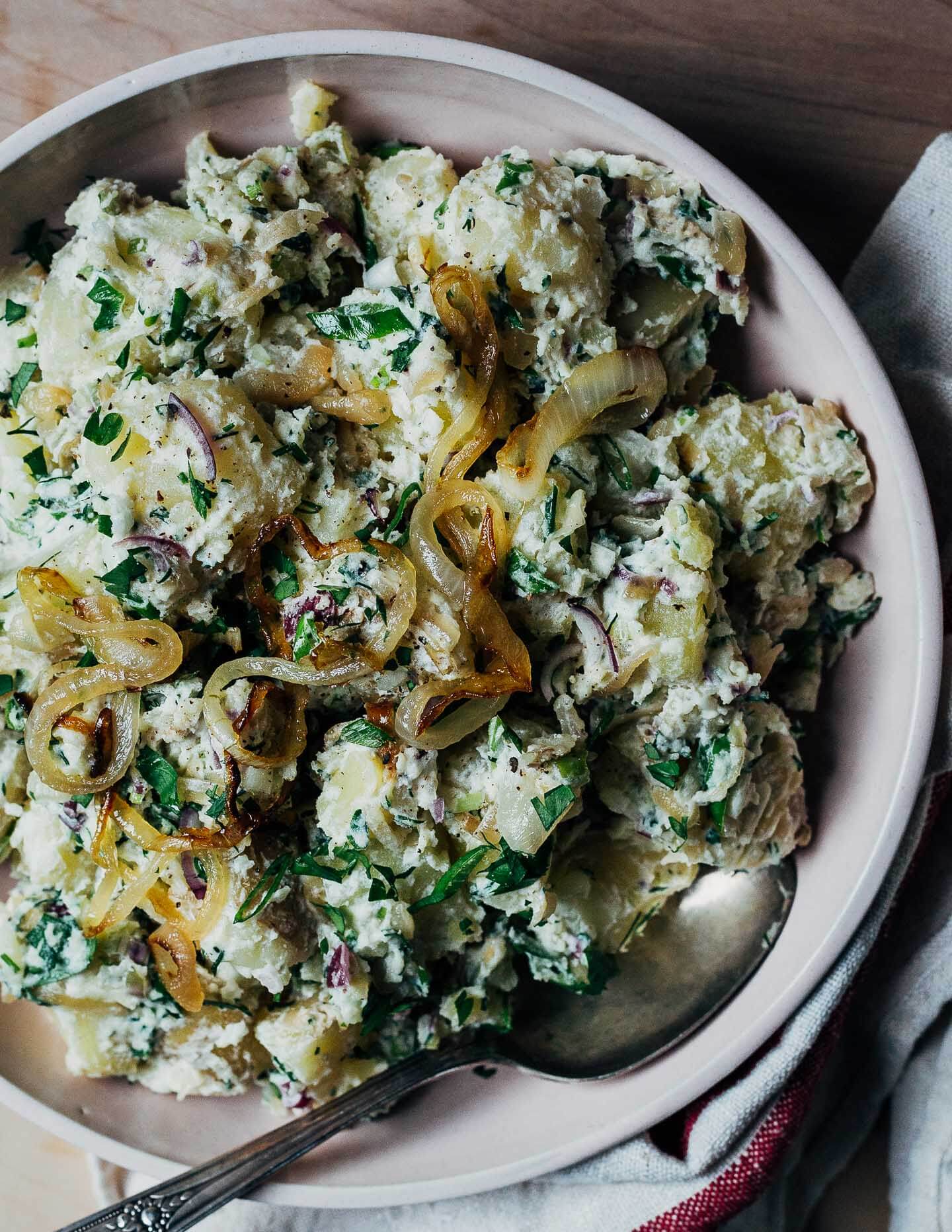 A bowl of potato salad with a serving spoon and a dish cloth. 