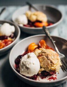 Bowls of cherry and peach cobbler with scoops of vanilla ice cream.