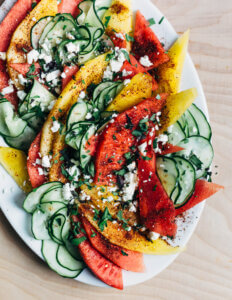 A platter of cucumber and watermelon salad with sumac, crumbled cheese, herbs.