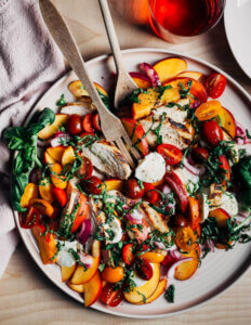 A platter with a colorful chicken caprese salad with herbs, peaches, and mozzarella.