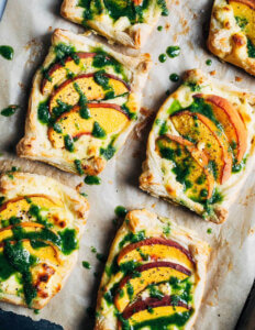 Little peach tarts drizzled with green basil oil on a baking sheet.