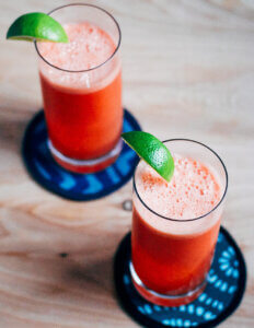 Two glasses of frothy watermelon coolers garnished with a wedge of lime.