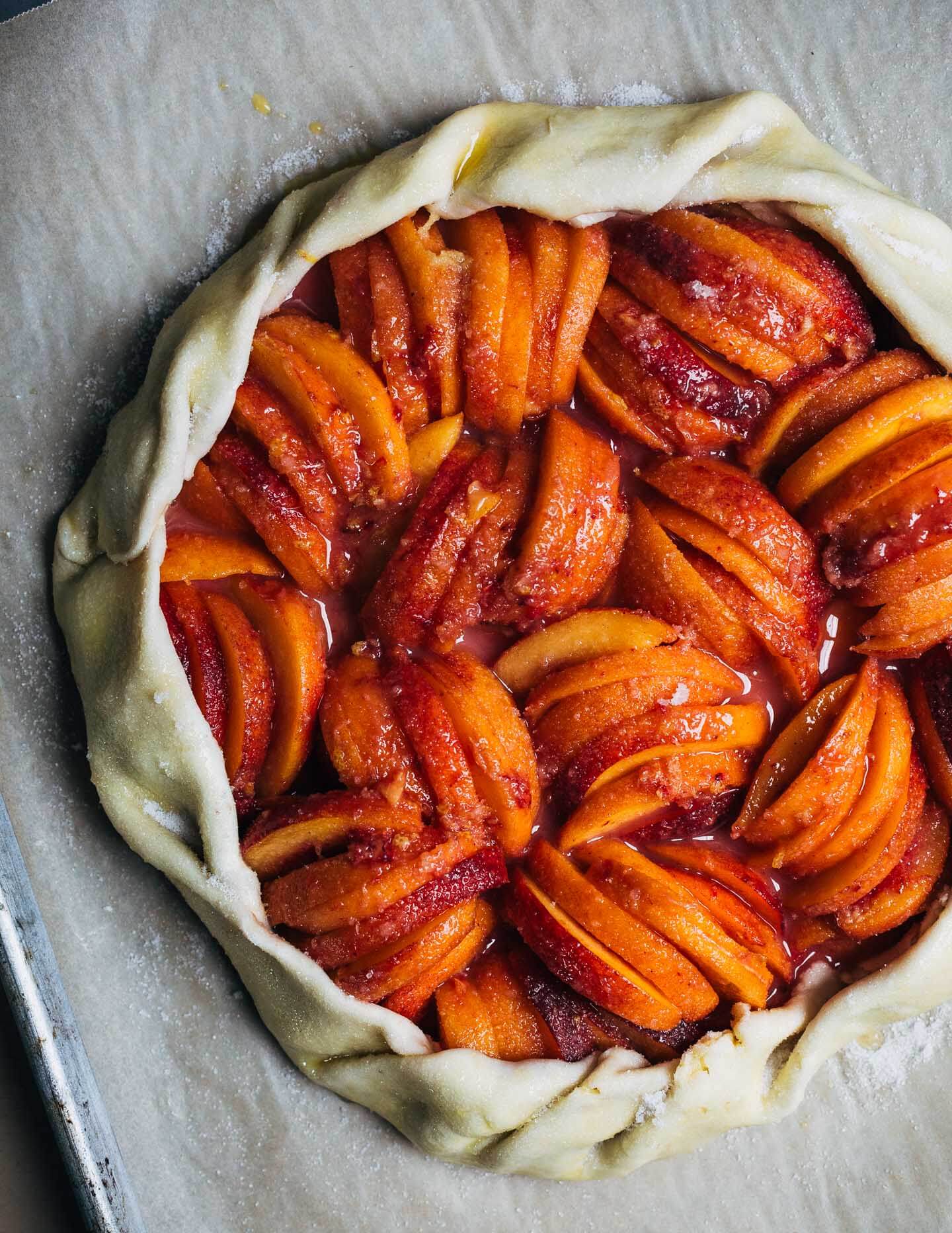 A peach galette on a baking sheet, crimped and ready to bake. 