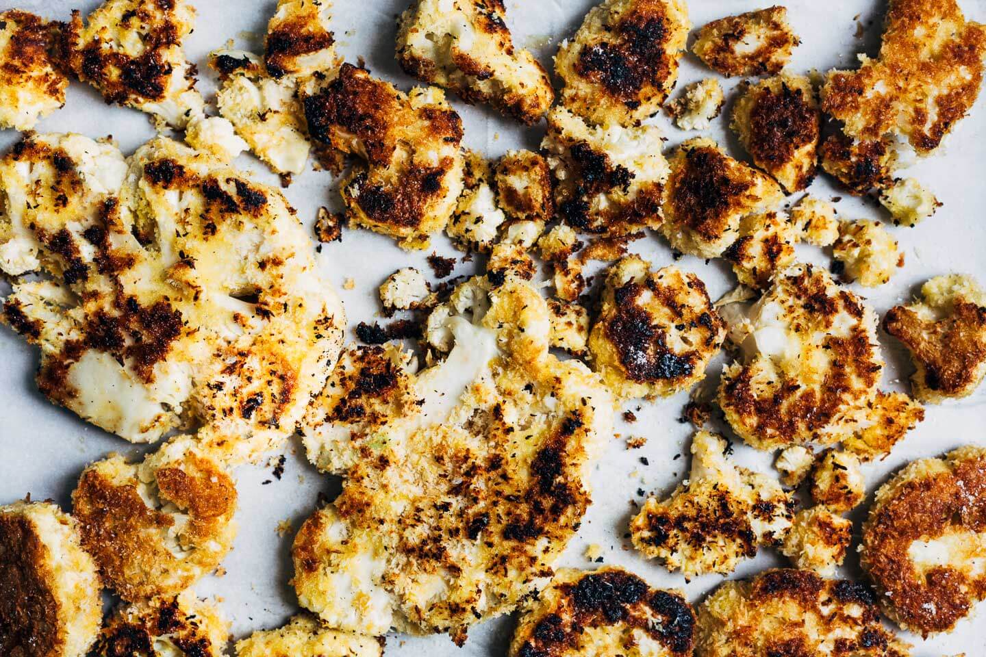 Breaded, fried cauliflower on a parchment-lined baking sheet. 