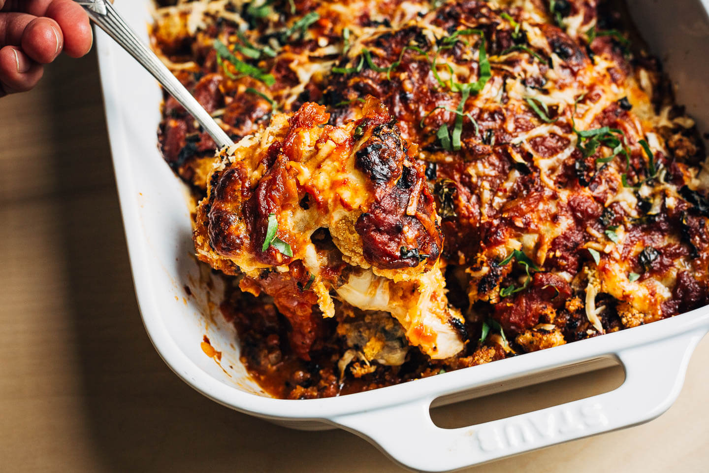 A serving spoon lifting the melty cauliflower Parmesan out of the baking dish. 