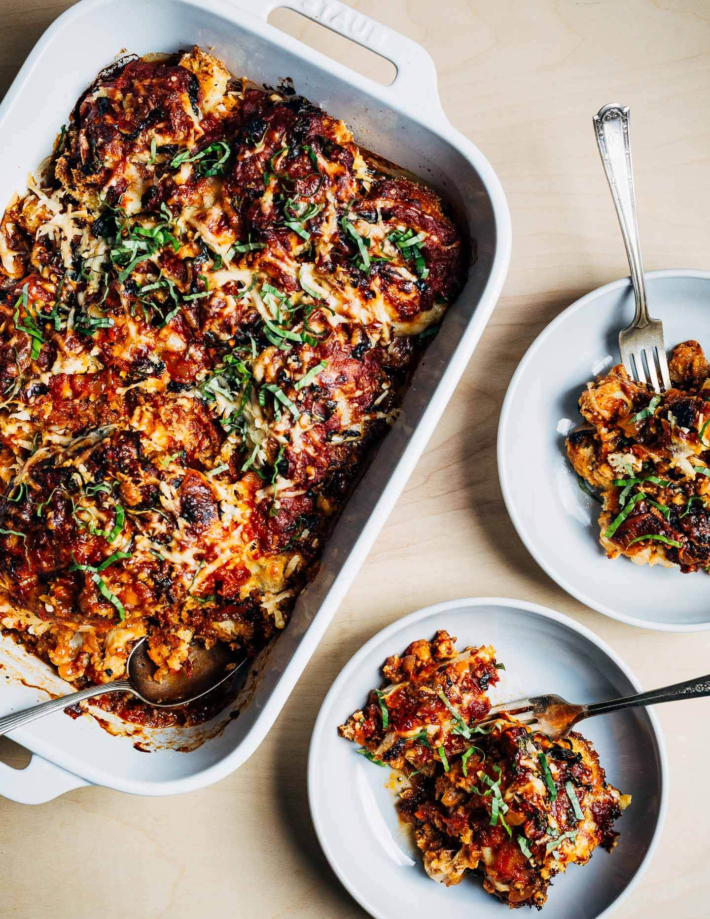 A baking dish of cauliflower Parmesan alongside two plated servings. 