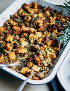 A baking dish with cornbread stuffing and a serving spoon alongside.