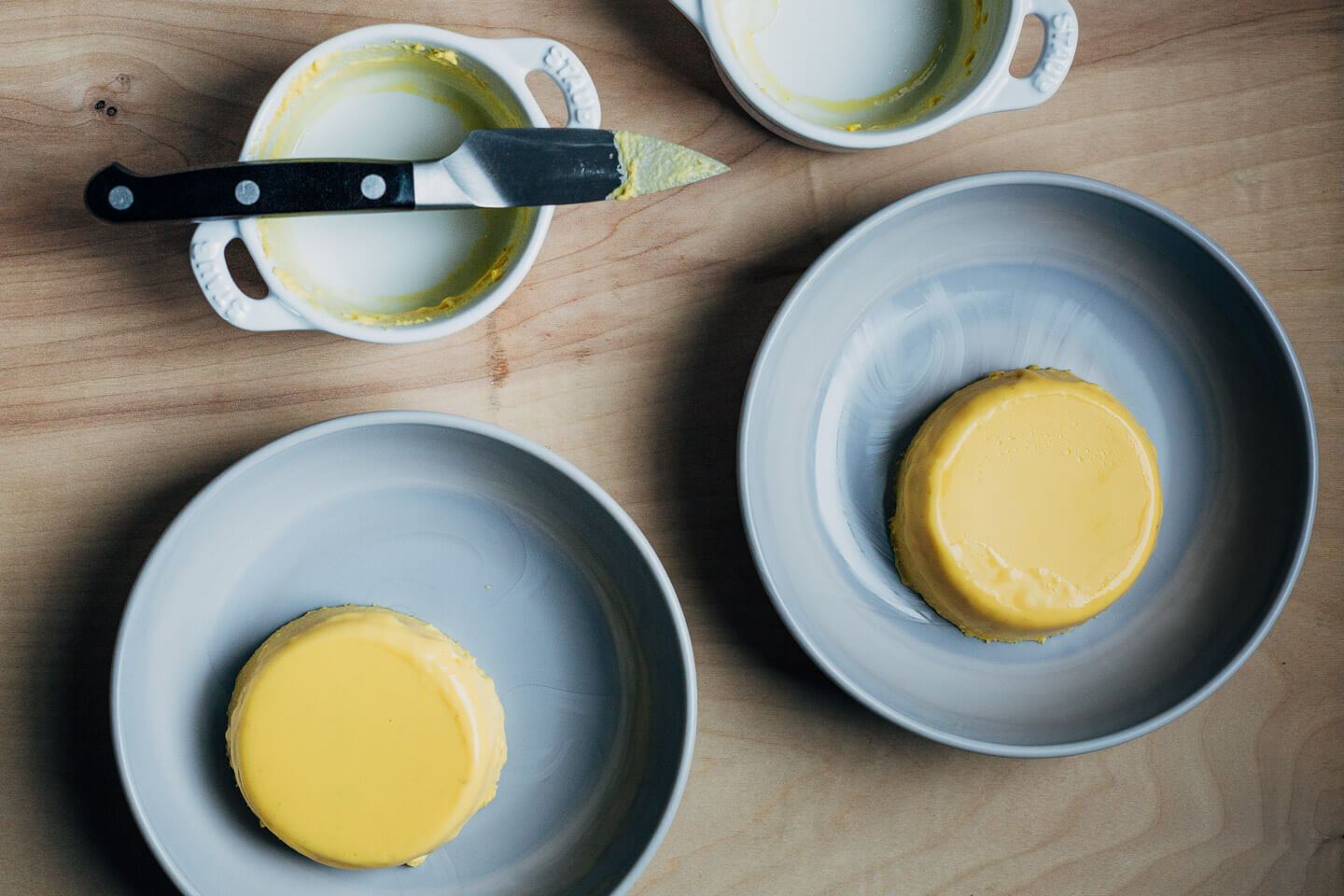 Unmolding panna cotta on a table – there are two plated desserts, two empty ramekins, and a knife. 