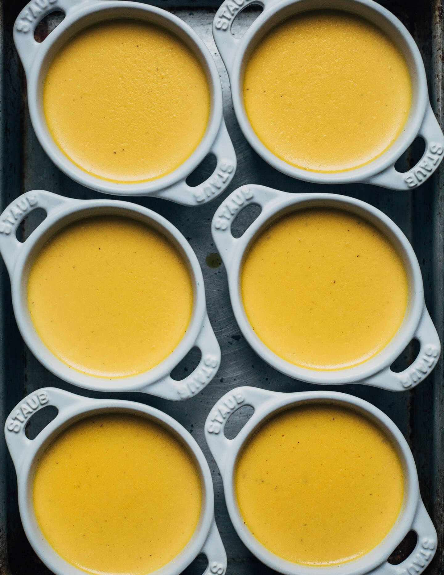 Little ramekins filled with panna cotta on a tray. 