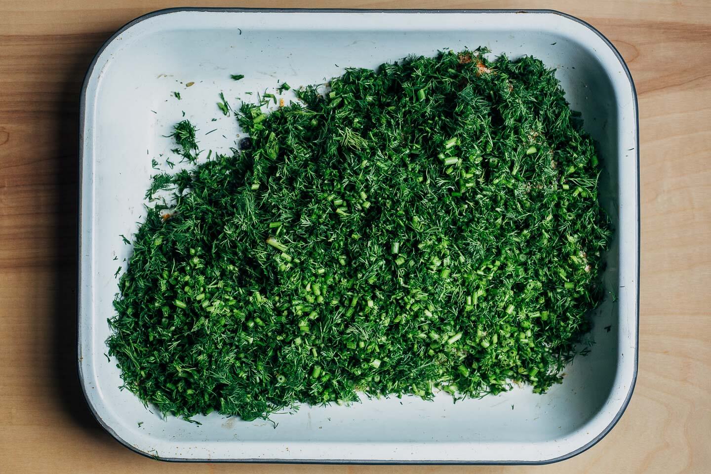 A salmon filet covered in dill and a salt, sugar, and spice mixture for curing. 