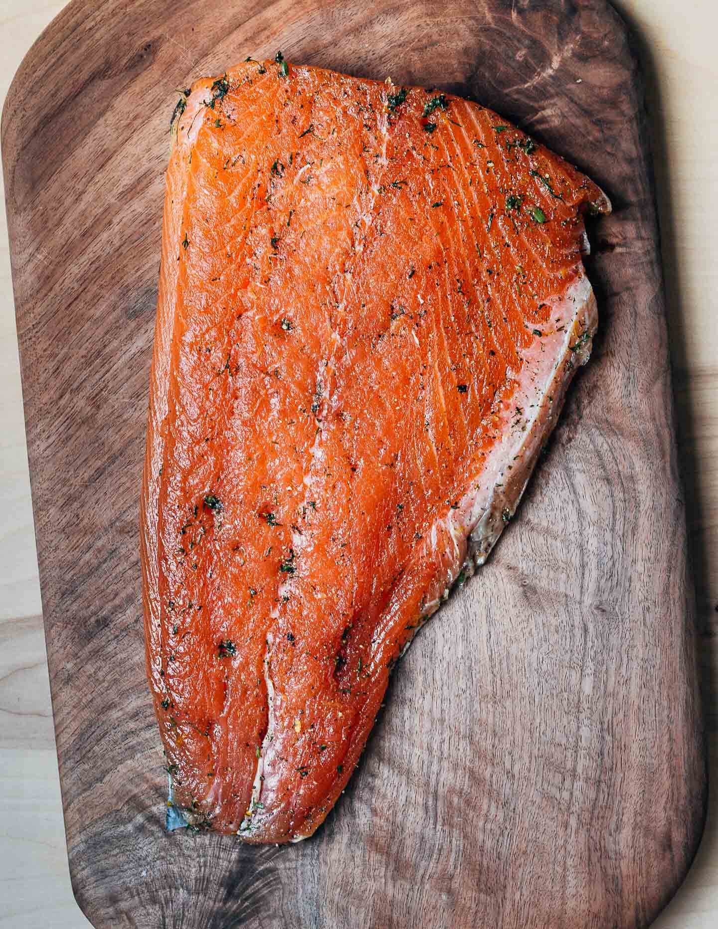 Cured gravlax sitting on a dark wood cutting board. 