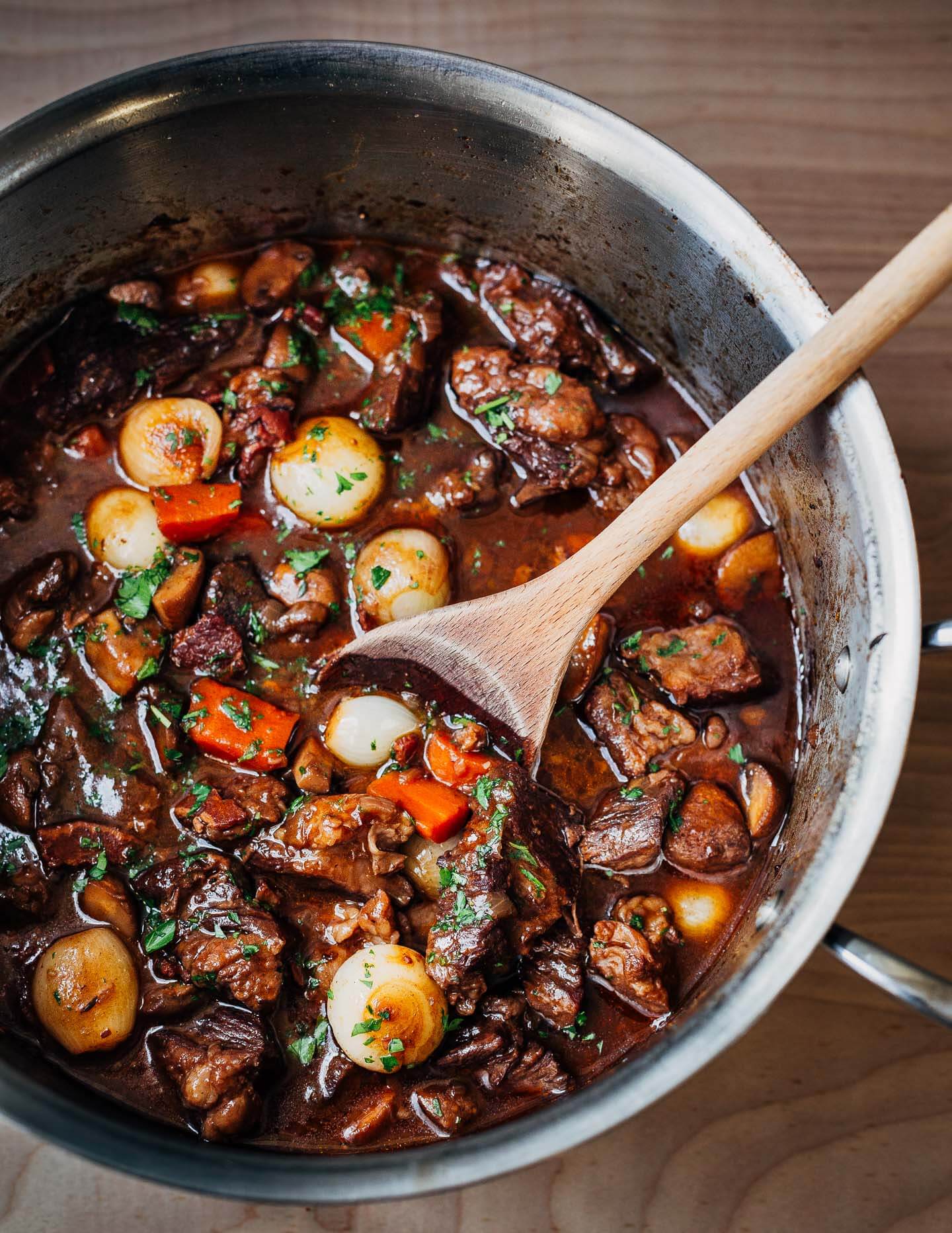 A pot of beef Bourguignon being stirred by a spoon. 