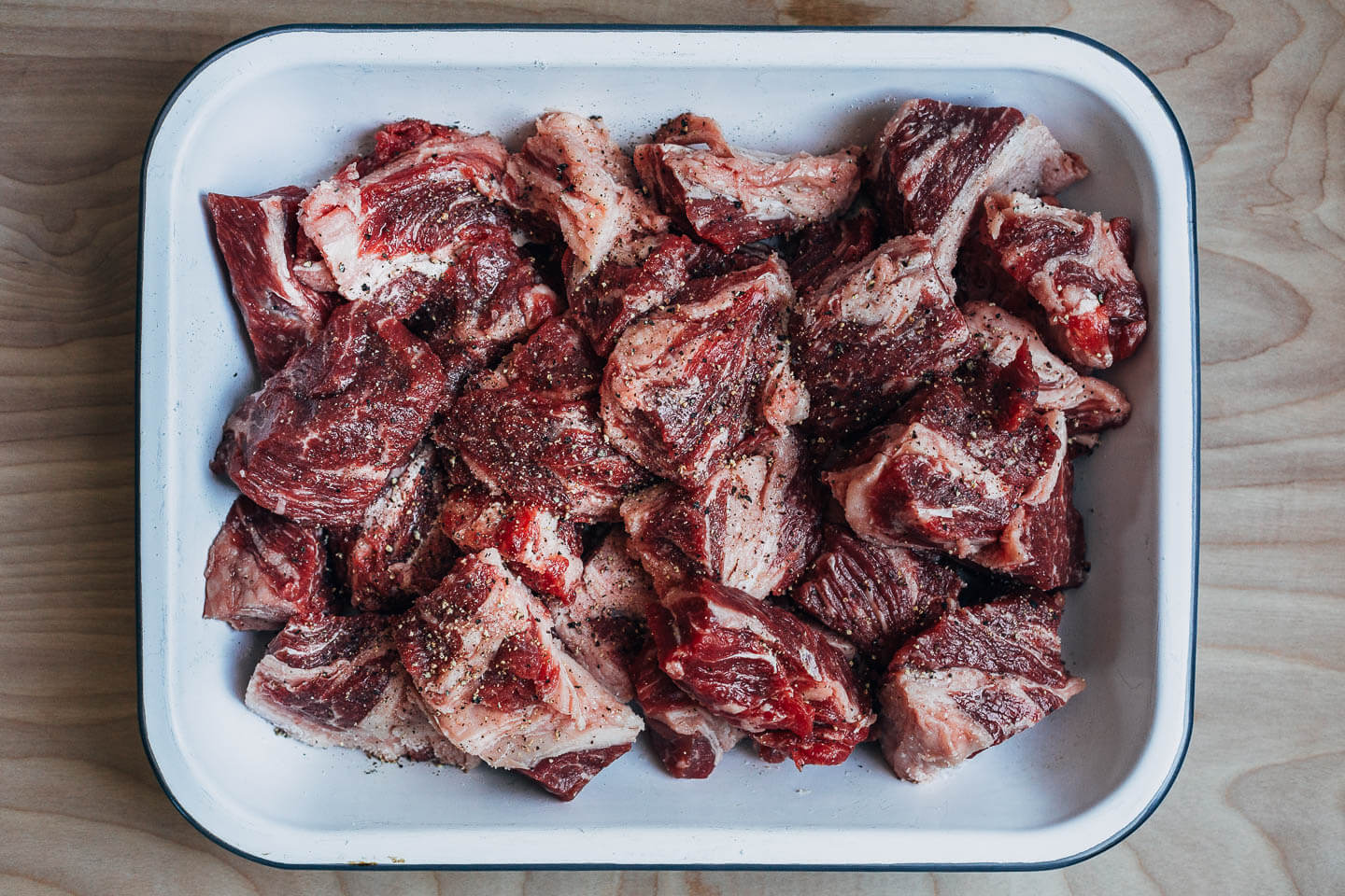 A pan with cubed pieces of beef sprinkled with salt and pepper. 