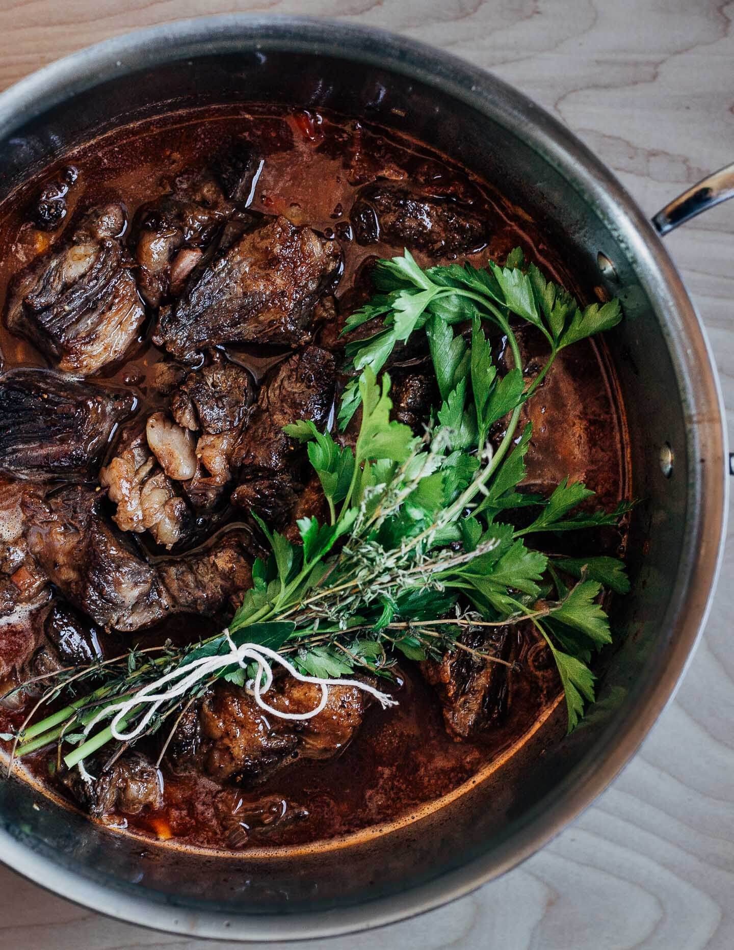 A pot with seared beef, wine and broth, and the bouquet garnis, ready for the oven. 