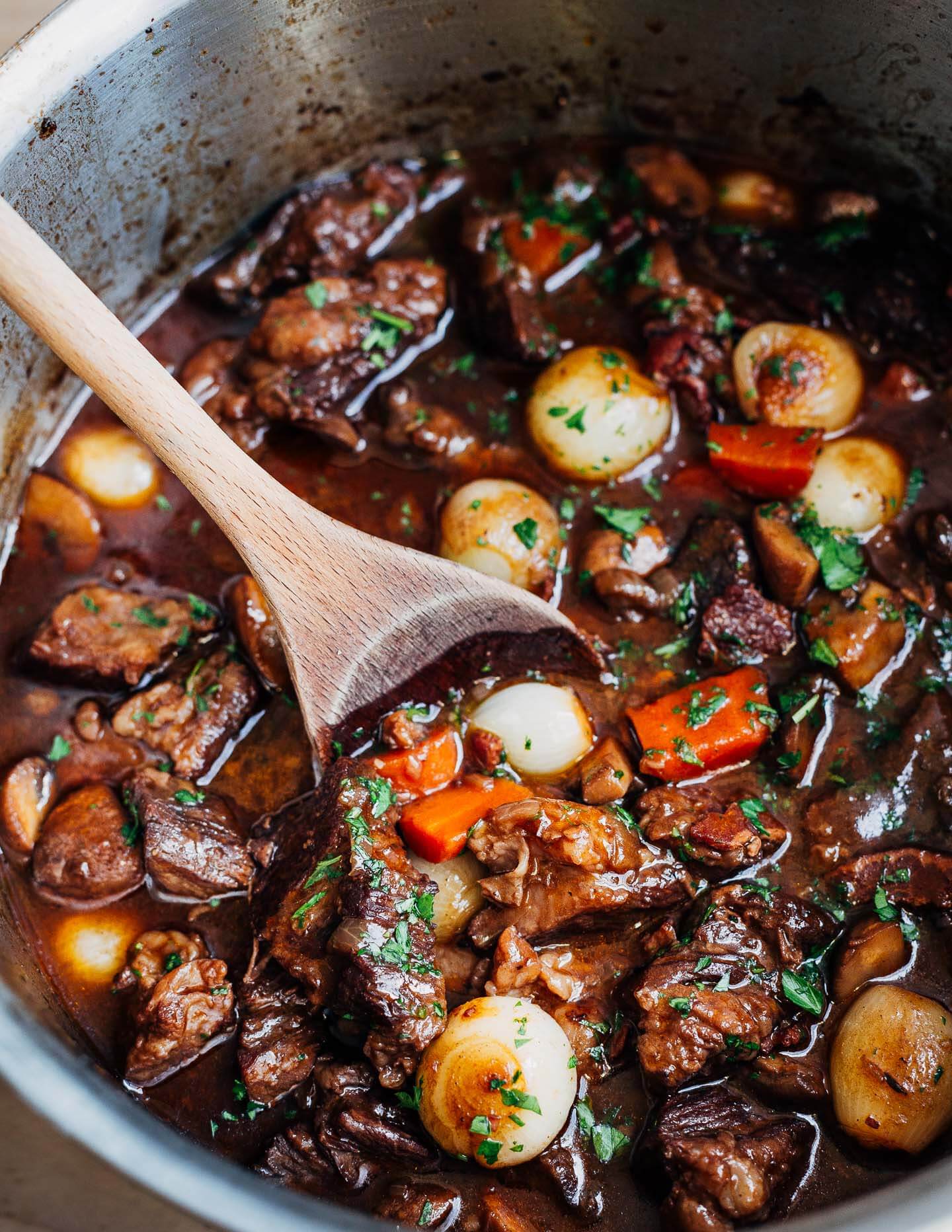 A pot of beef Bourguignon being stirred by a spoon. 