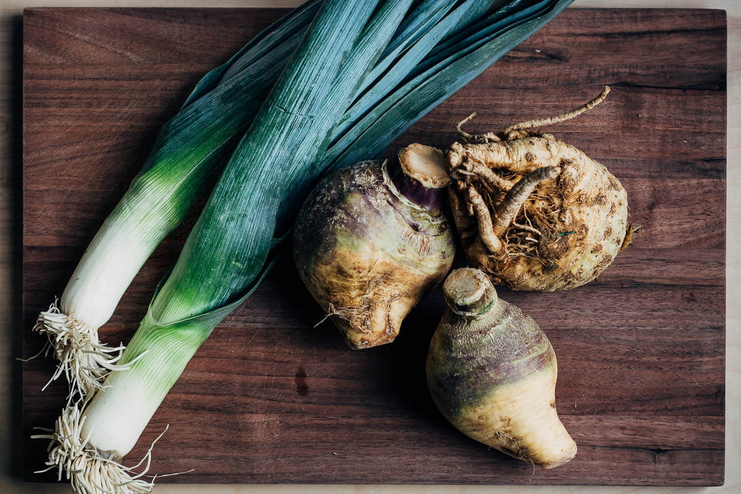 Leeks, celery root, and rutabagas on a cutting board.
