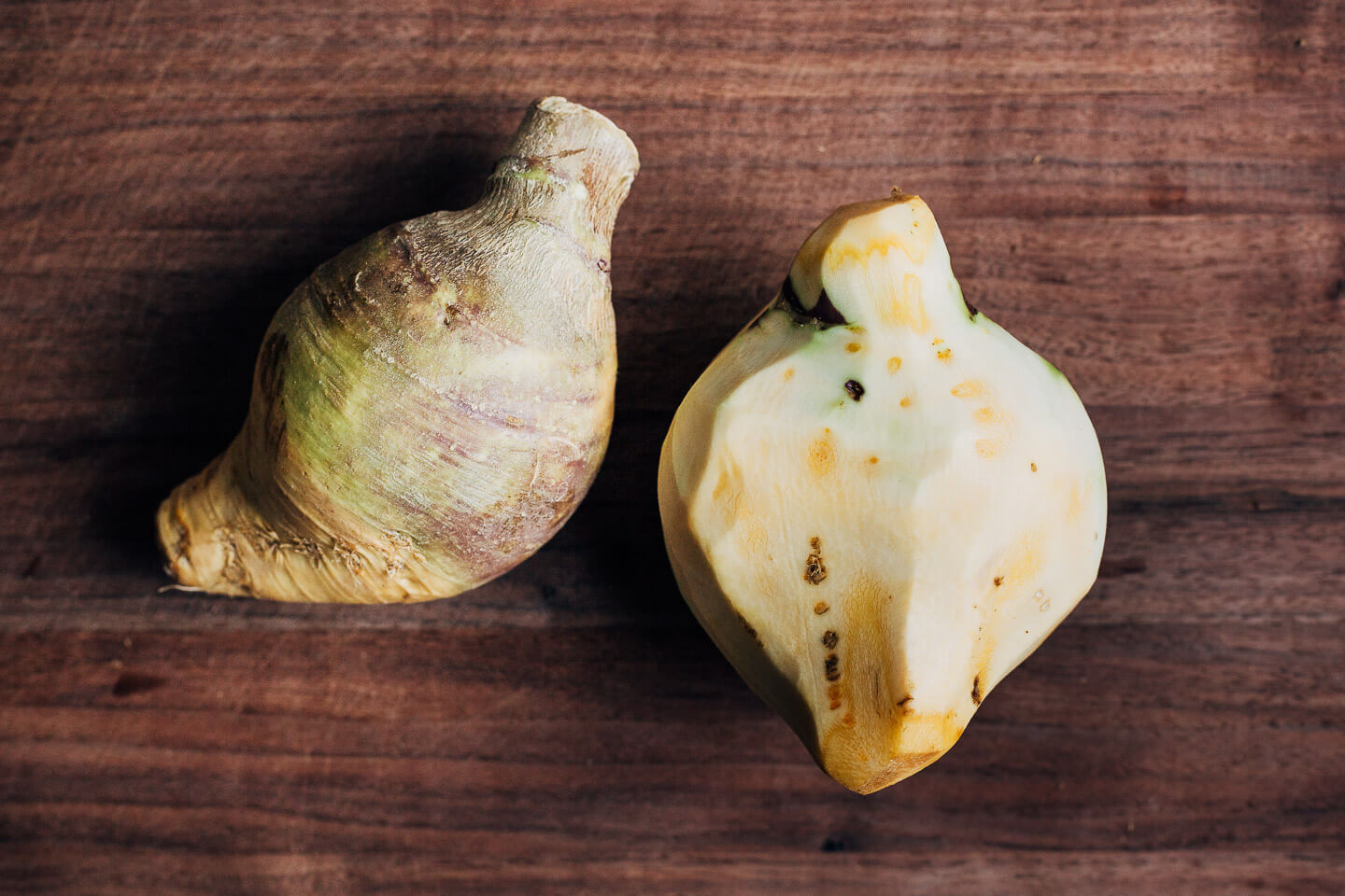 A peeled rutabage alongside an unpeeled one on a cutting board. 