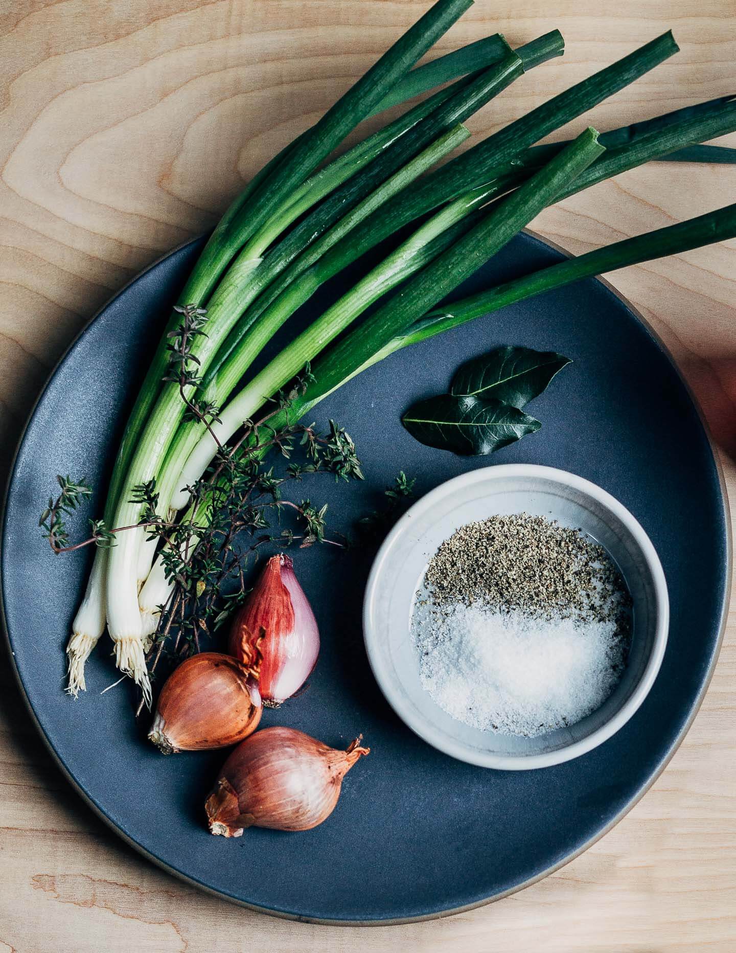 A dark gray plate with green onions, shallots, thyme, and a bowl of salt and pepper. 